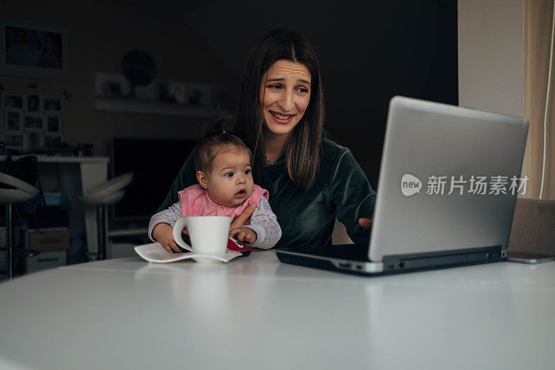 这位女士正试图在膝上抱着孩子的情况下完成她的笔记本电脑工作。