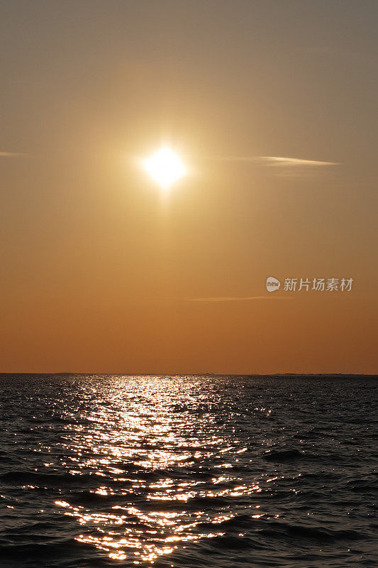 太阳在海上地平线上戏剧性的橙色天空中落下的图像，太阳在水中的反射，海面上的波浪，波涛汹涌的水面，复制空间