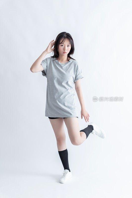 一位身穿灰色t恤和黑色短裤的年轻亚洲女子在白色背景上摆姿势