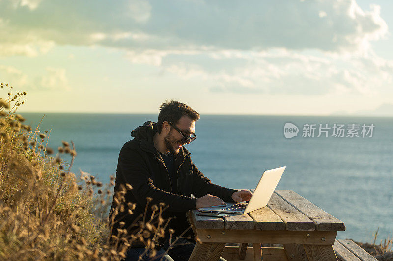 年轻的商人坐在大自然的木桌边用笔记本电脑工作