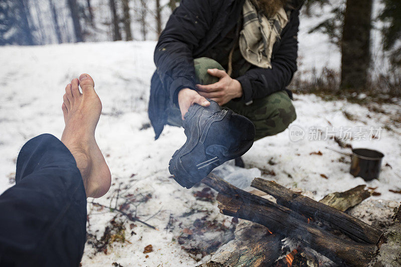 走过积雪森林后，成年男子正在晒脚和鞋子