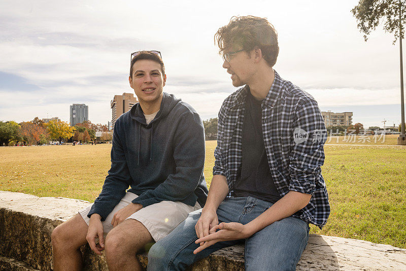 两个30岁左右的男性朋友，拉丁裔和白种人，在公园里坐着聊天