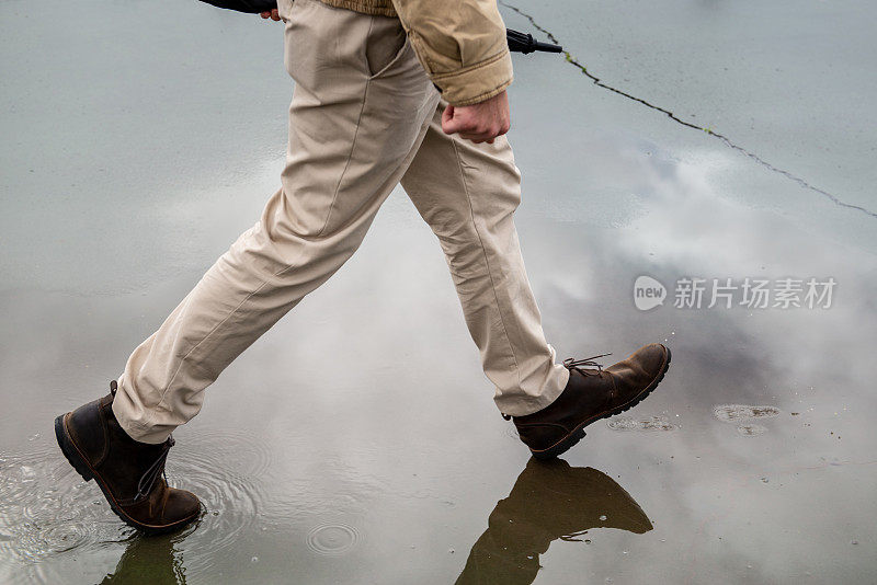 一名男子撑着伞在潮湿的柏油路上行走