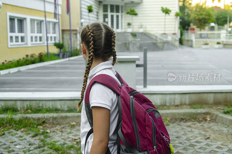 小女孩看着教学楼入口，准备上课。背着书包，穿着校服的女学生