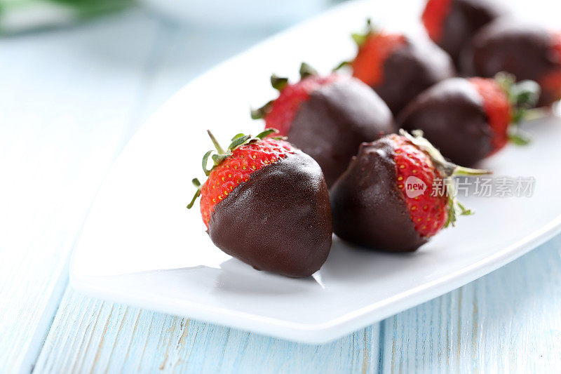 新鲜的草莓蘸黑巧克力放在蓝色的木背上