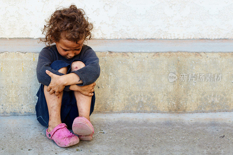 可怜而悲伤的小女孩靠在水泥墙上