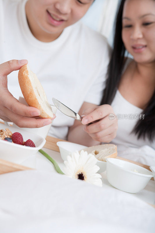 一对亚洲年轻夫妇在床上吃早餐