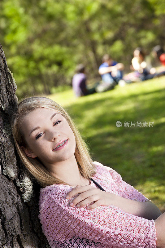 青少年:快乐的女孩在树下与朋友的背景