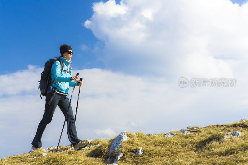 在蓝色多云的天空下，穿着徒步旅行装备的女人