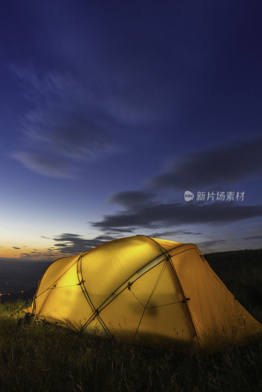 在蓝色的黄昏天空下，五颜六色的山帐篷在山顶发光