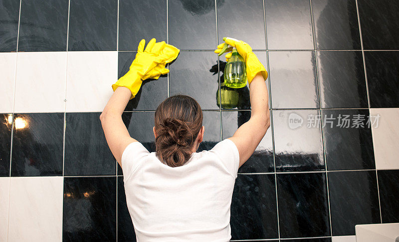 女人清洁浴室瓷砖，后视图