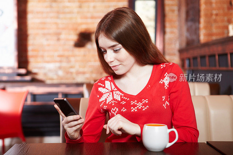美丽的女孩在咖啡厅拿着手机短信。