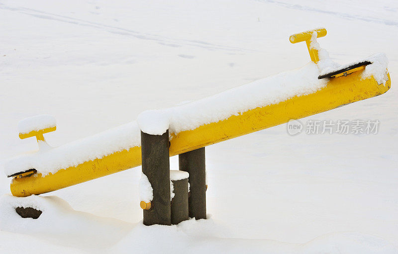 黄色的跷跷板在儿童游乐场的雪地里