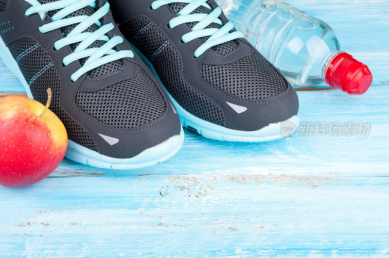 运动器材和运动鞋。运动鞋，苹果，蓝色木制背景上的一瓶水。健康的生活方式，健康的食品，运动和饮食的概念