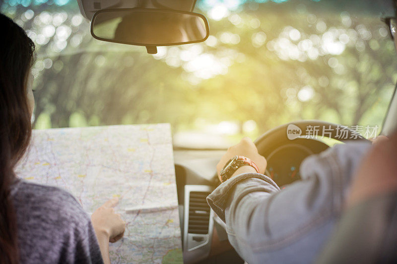 亚洲男人和女人使用地图公路旅行和快乐的年轻夫妇与地图在车里。模糊和柔焦