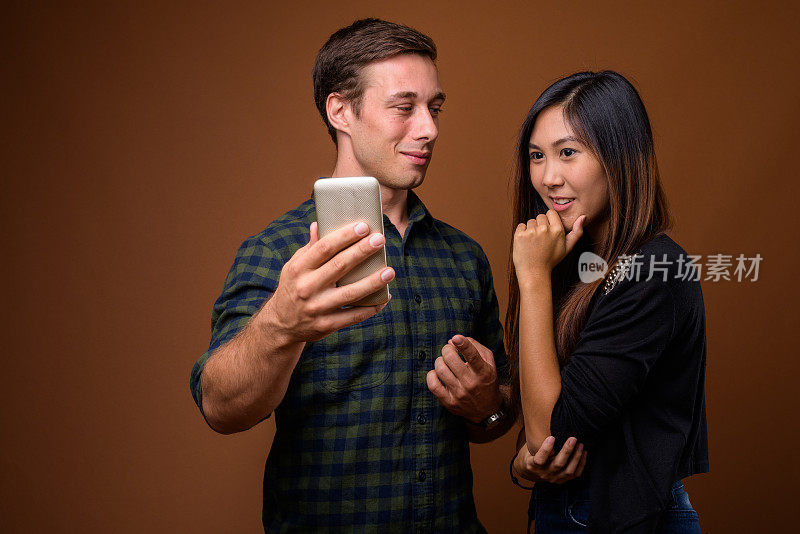 工作室拍摄的年轻英俊的男子和年轻美丽的亚洲女子一起使用手机以彩色背景