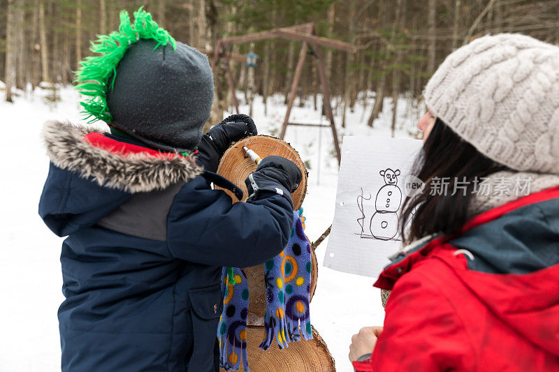 母亲和儿子在冬天户外做一个木制雪人