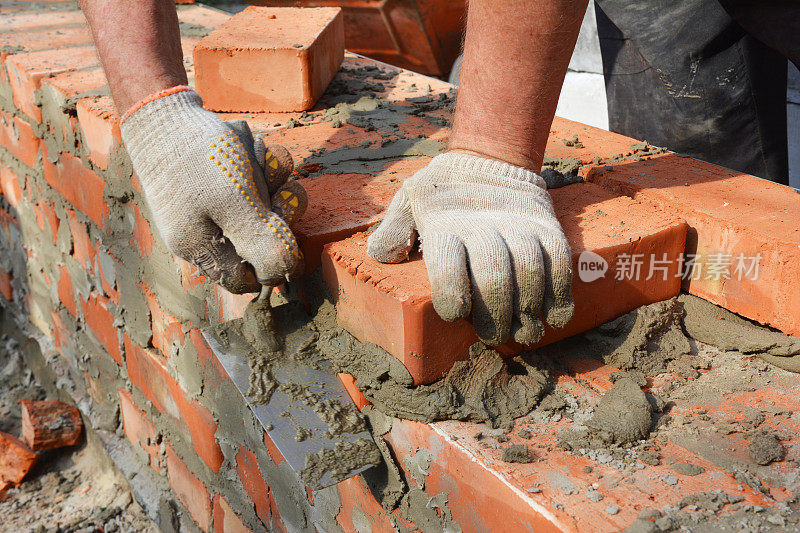 泥瓦匠双手戴着砖石手套在砌砖新房子的砖墙。砌体密切起来。