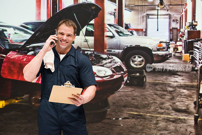 白人男性汽车修理工在汽车修理店穿着工作服拿着文件用智能手机修理