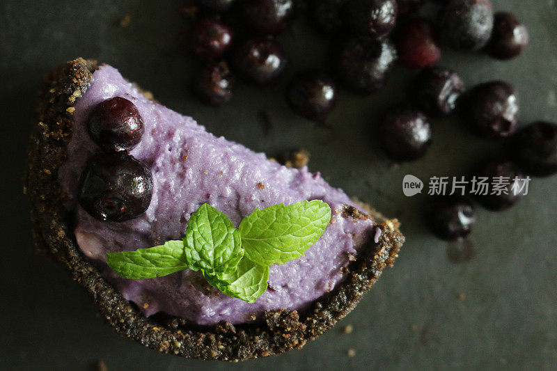 这是一个微型蓝莓芝士蛋糕，底部是黄油饼干，周围是浆果，半块蓝莓马斯卡彭奶油芝士甜点布丁，上面点缀着新鲜的蓝莓和薄荷叶