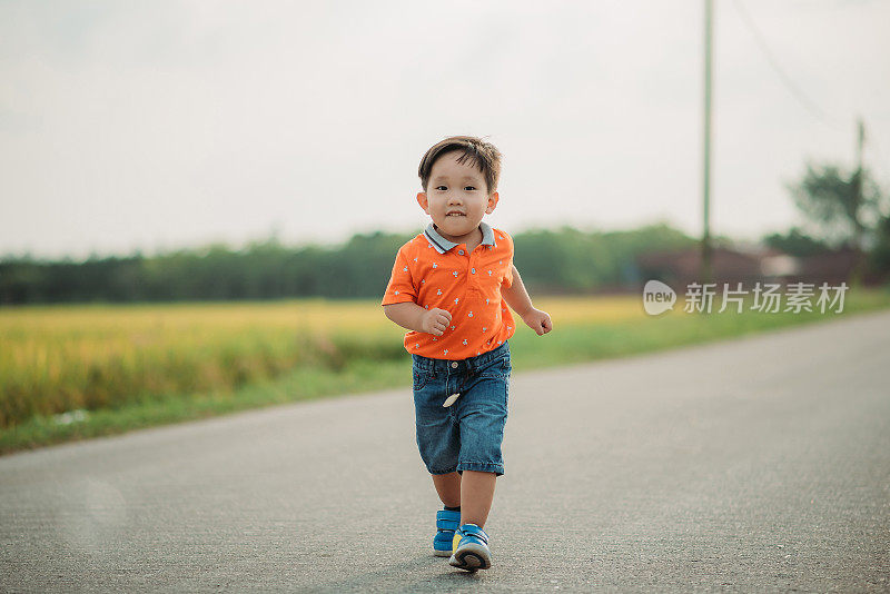 亚洲华人微笑男孩花闲暇时间，在村里的街道上跑步