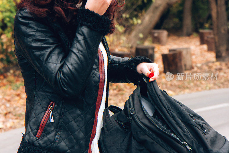 一个穿着皮夹克的年轻女子把东西放在背包里，背景是秋天森林里的一条自行车道