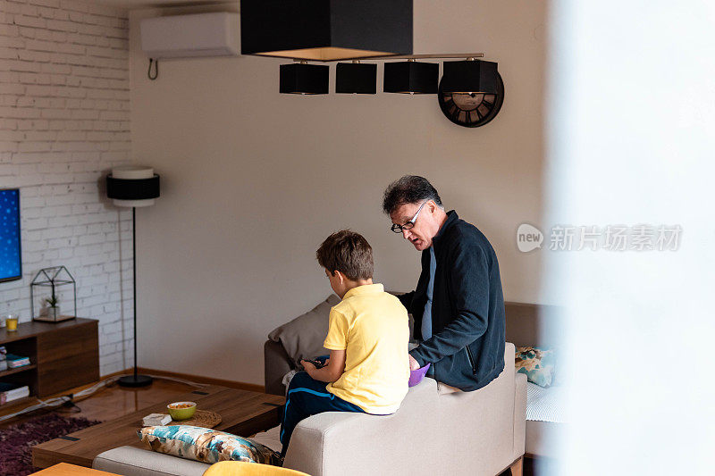 爷爷和孙子坐在客厅的沙发上看电视
