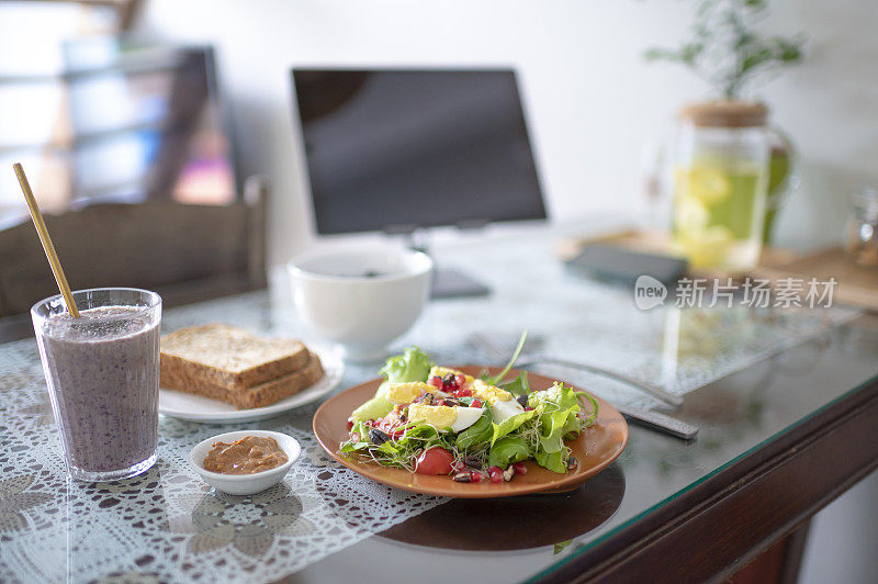 早餐健康食品沙拉，水果奶昔，烤面包在餐桌上与数字平板电脑