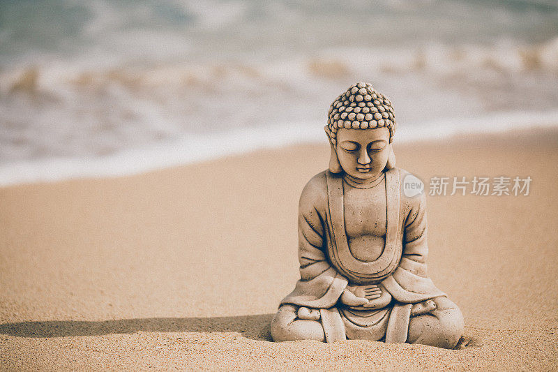 美丽的佛像坐在海边的石像上，海浪在海滩上迎面而来