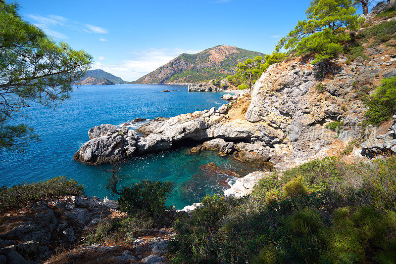 从山上眺望蔚蓝的地中海和松树，山坡上有岩石，天空湛蓝