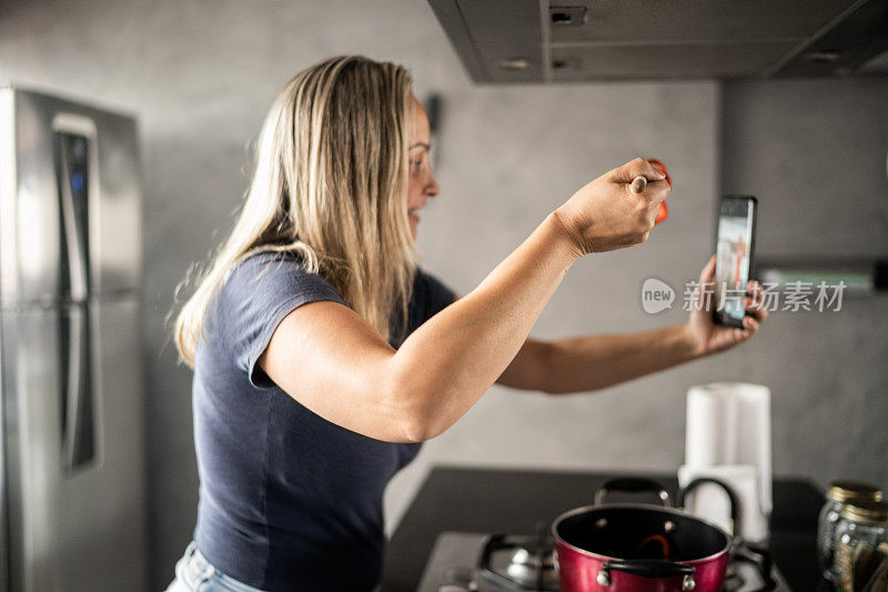 成熟的女人做饭和展示食物在视频通话在家里的智能手机