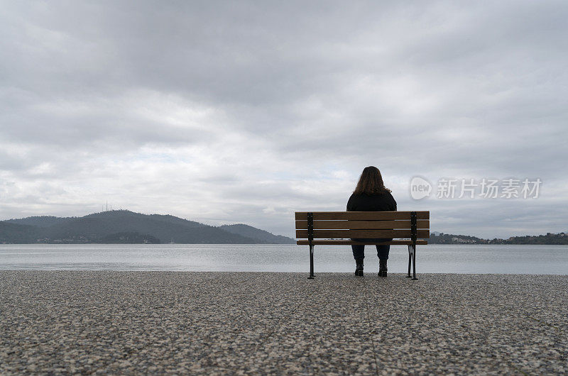 一个超重的年轻女人坐在海边的长椅上看风景