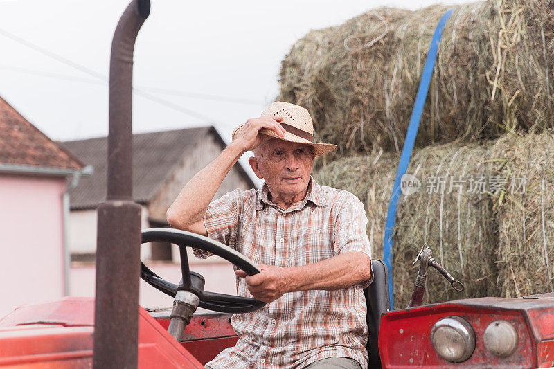 老农开着拖拉机，手里拿着草帽