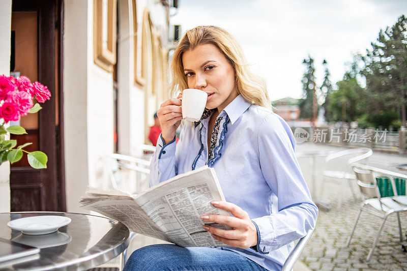 一个年轻漂亮的女人正在一家咖啡馆的花园里喝她的早晨咖啡。