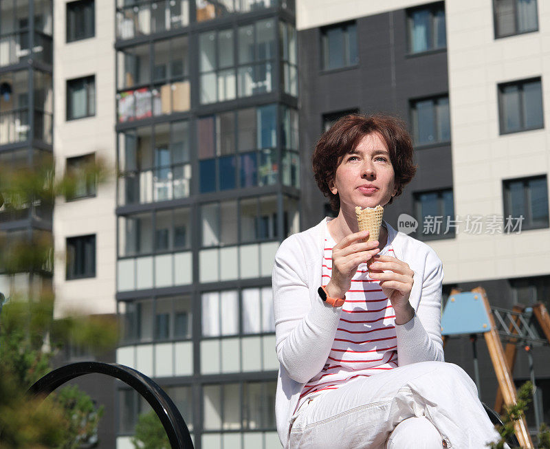 一个女人坐在城市街道的长椅上，吃着冰淇淋蛋筒