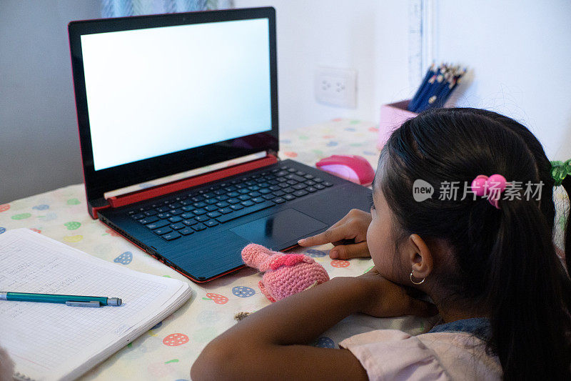 一个小女孩在家里用笔记本电脑facetime视频通话，使用在线虚拟课堂缩放，社交距离，家庭教育，远程学习
