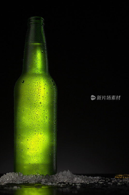 冰凉的绿色啤酒瓶，上面覆盖着冰和水滴-凝结。用于饮料饮料产品设计模型的毛坯。站在黑色背景的黑色桌子上。