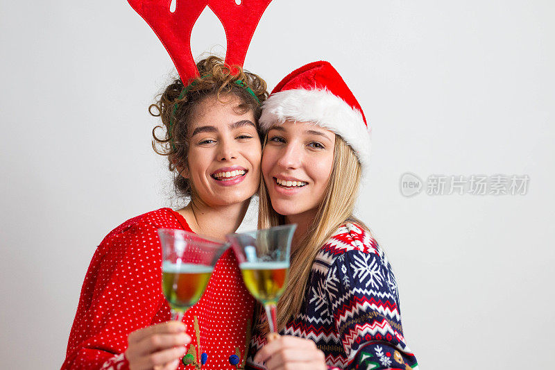 为新年干杯!两个穿着新年毛衣，戴着新年帽的女人