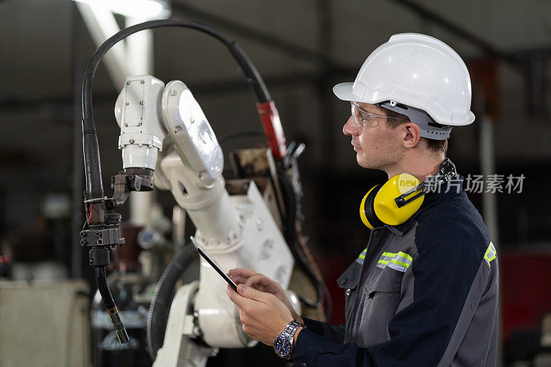 男工程师工人在工厂使用数码平板电脑控制自动机械臂机器。男技术员工人在智能工厂用平板电脑维护自动机械手
