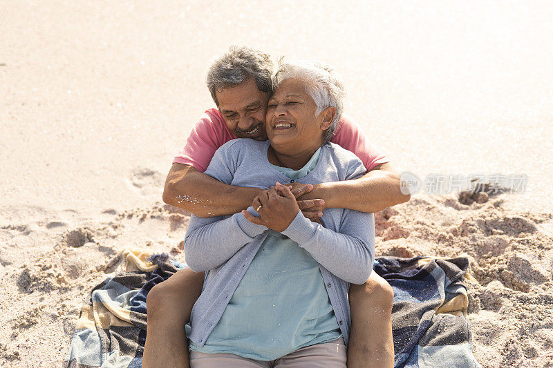 高角度的观点，爱的混血年长男子拥抱快乐的女人从后面坐在阳光海滩