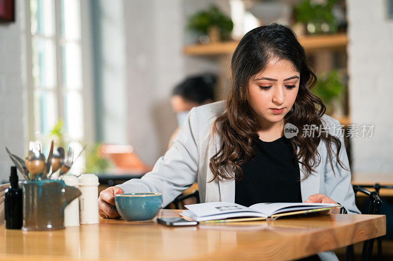 年轻的女商人在咖啡馆里看书喝咖啡。