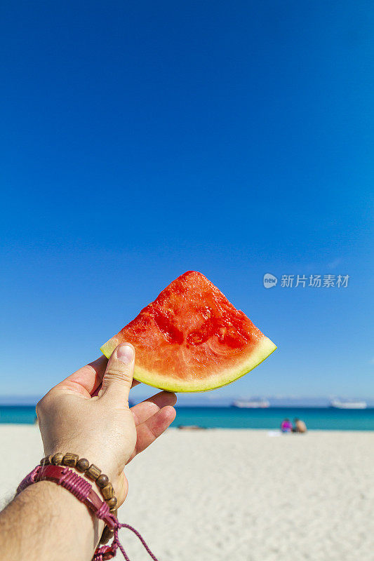 一名年轻的旅行男性在大西洋前享受他的假期，同时吃着健康的一块西瓜，南海滩，迈阿密海滩，迈阿密，南佛罗里达，美国