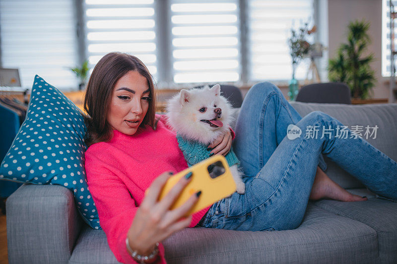 微笑的小女孩正在放松，抱着她的博美犬和自拍