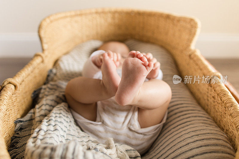 一个19周大的男婴躺在一个舒适的纱布毛毯里，躺在一个海草摩西篮子里