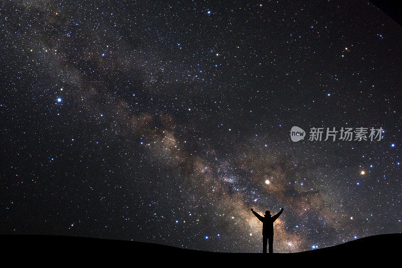 景观与银河，夜空与星星和一个站在高山上举起手臂的运动男子的剪影。
