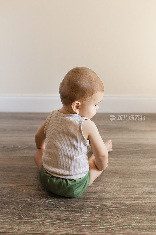 2022年，患有多指畸形的7个月大的男婴穿着橄榄绿可重复使用和可持续的布尿布和背心坐在家里的木地板上