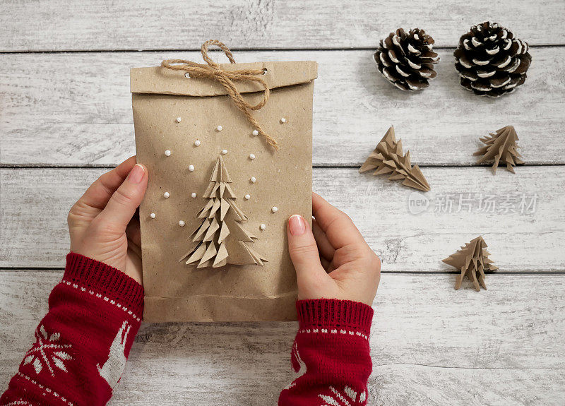 女人的手拿着用她们自己的手做的礼物袋。圣诞和新年礼物袋，装饰装饰。手工环保包装的礼物。纸张回收利用，零浪费