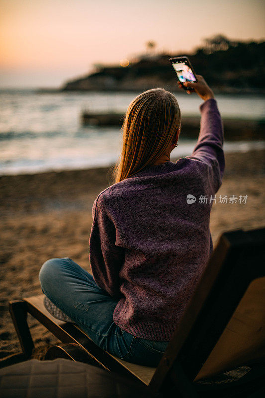 一名女子用智能手机在海滩上自拍日落