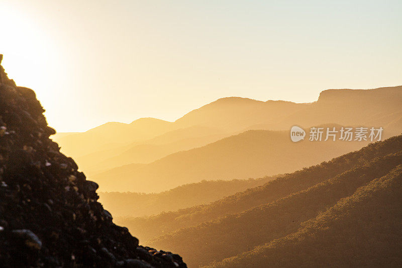 太阳在树梢上落下，在金色的光线中起伏的山景