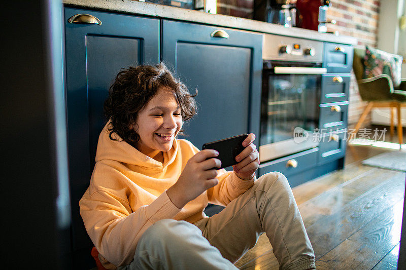 小男孩坐在厨房地板上玩智能手机